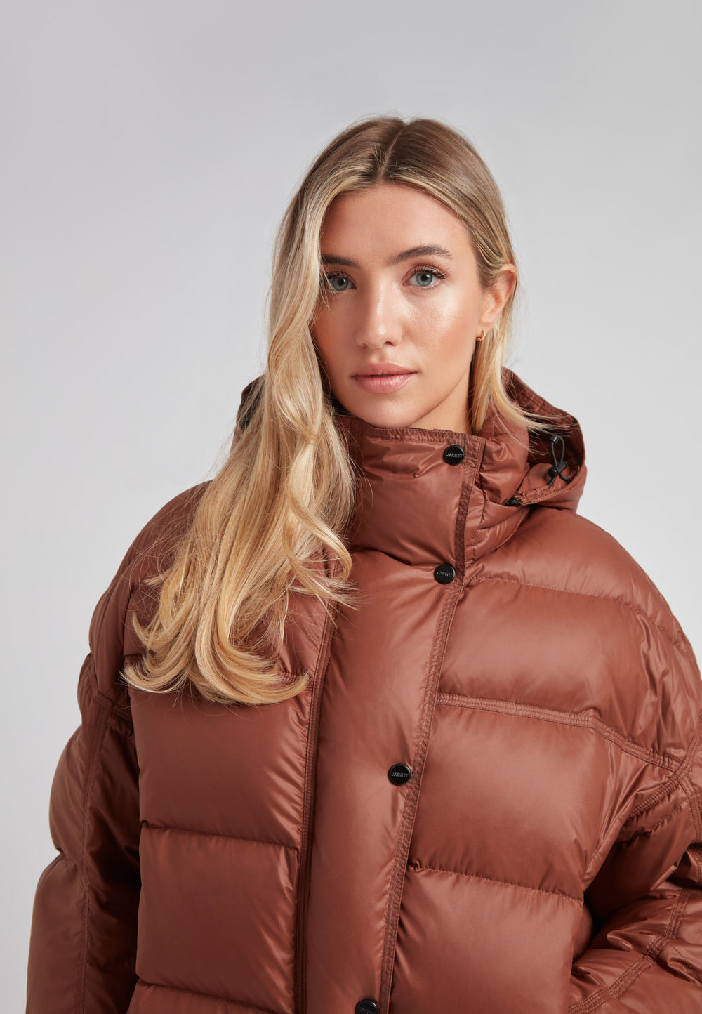 Cropped puffer in mocha brown with adjustable coverage, showcasing a model wearing a stylish oversized down jacket.