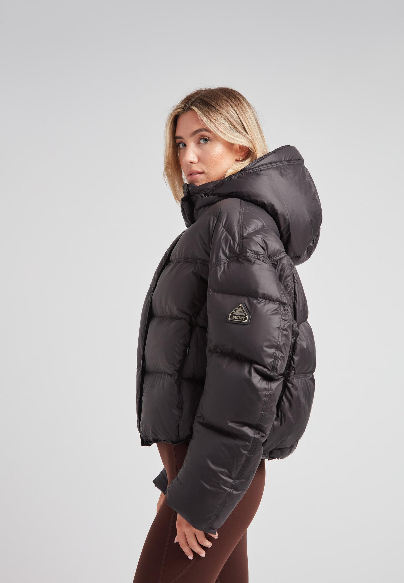 Cropped puffer in black with adjustable coverage worn by model, showcasing its oversized design and removable hood.