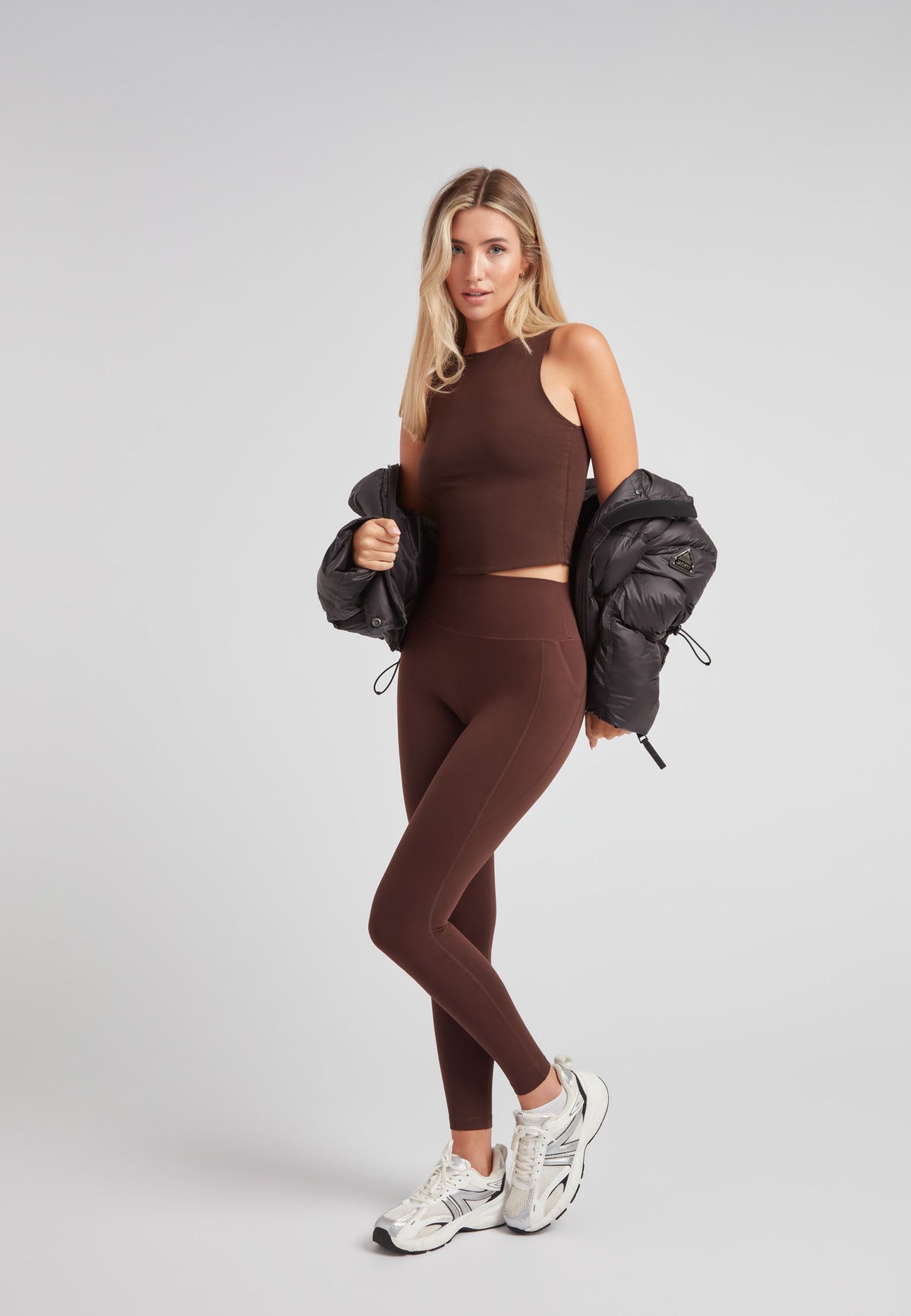 Model wearing a cropped puffer in black with adjustable coverage, styled with brown activewear.