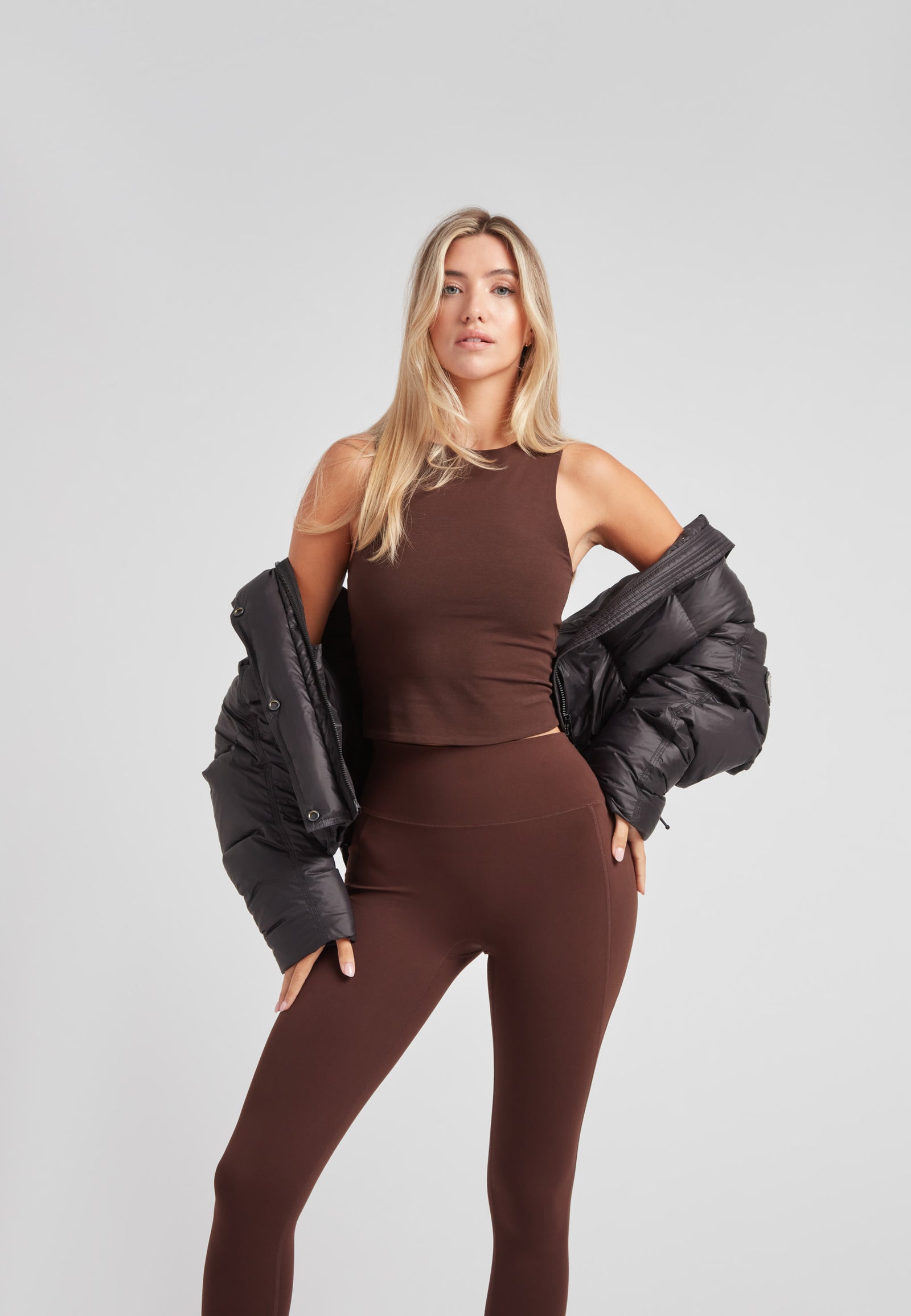 Model wearing a cropped puffer in black with adjustable coverage over a brown athleisure outfit.