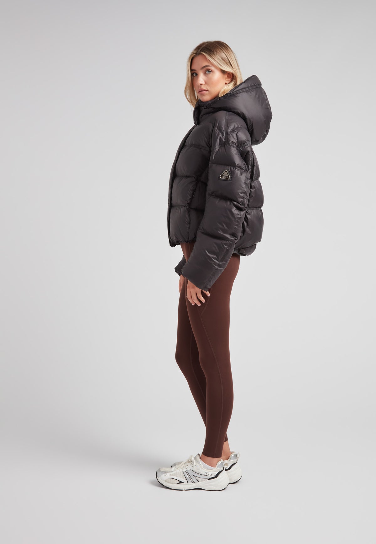 Cropped puffer in black with adjustable coverage worn by model with brown leggings and sporty shoes.