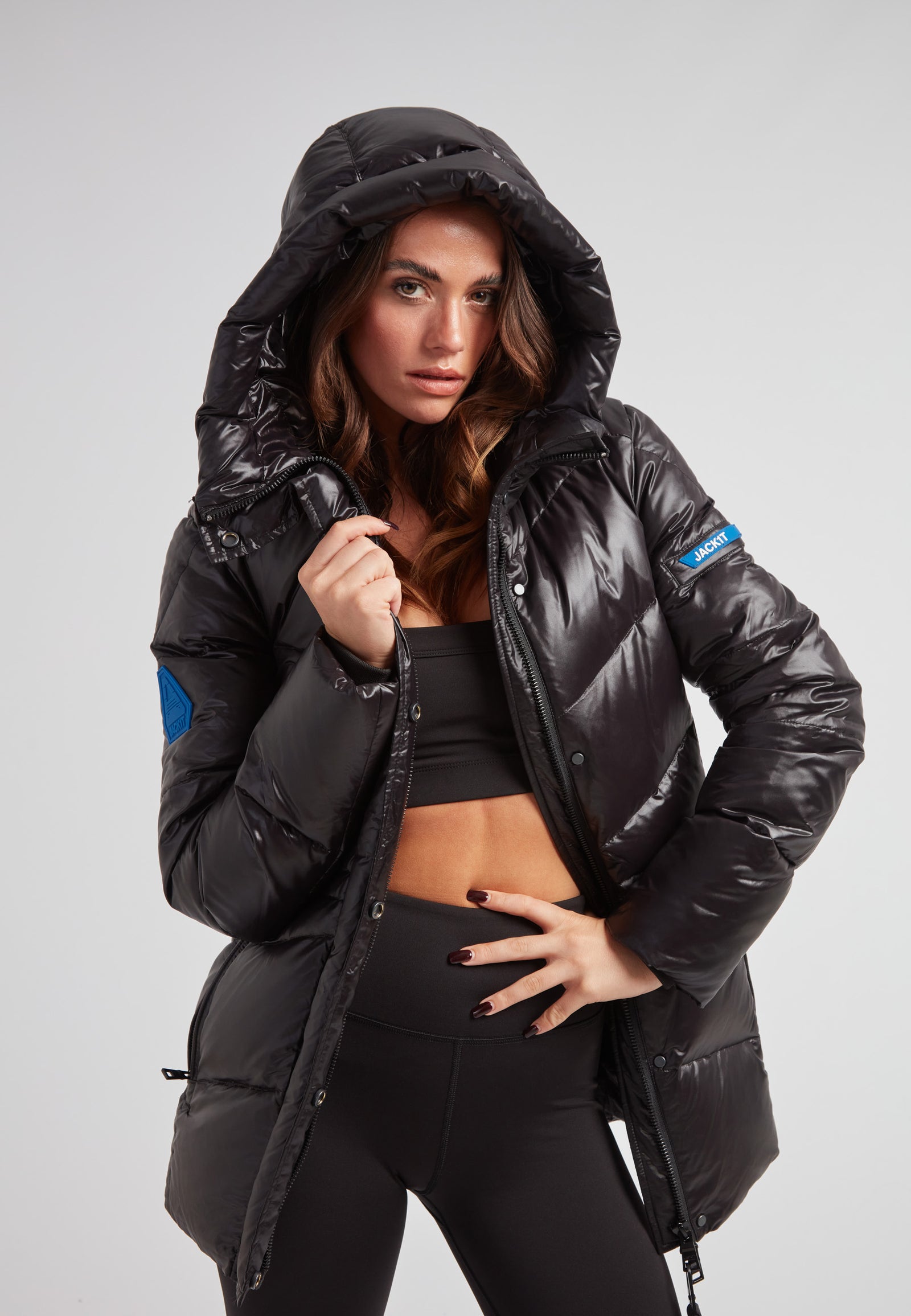 Model wearing black thigh-length womens slick coat with hood, showcasing its stylish puffer design and glossy finish.