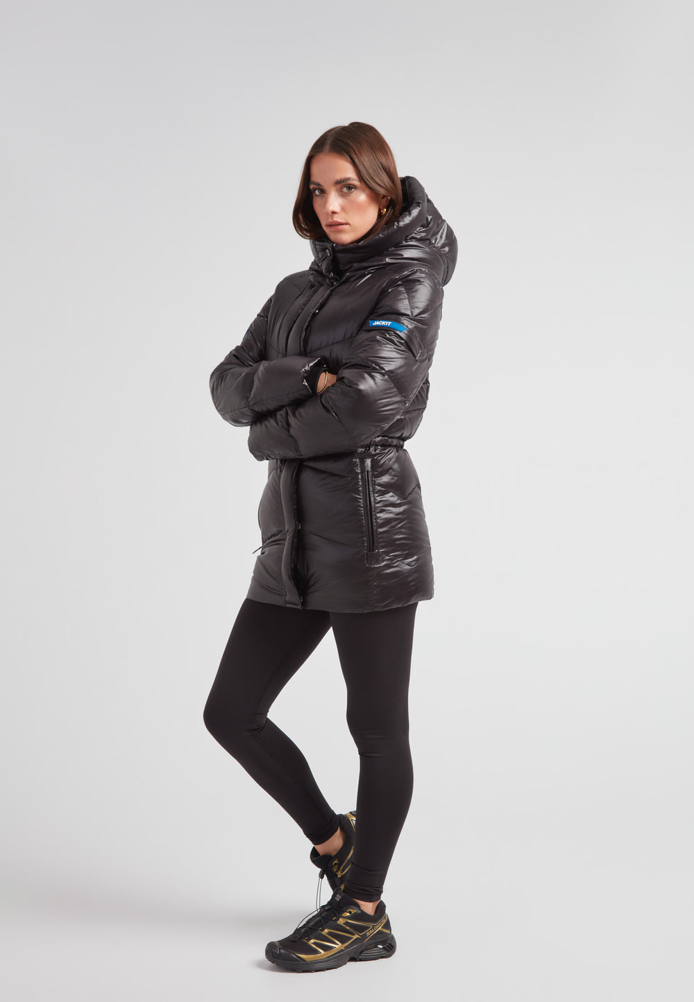 black thigh-length womens slick coat on model with arms crossed and hood up, showcasing stylish design and warm insulation.