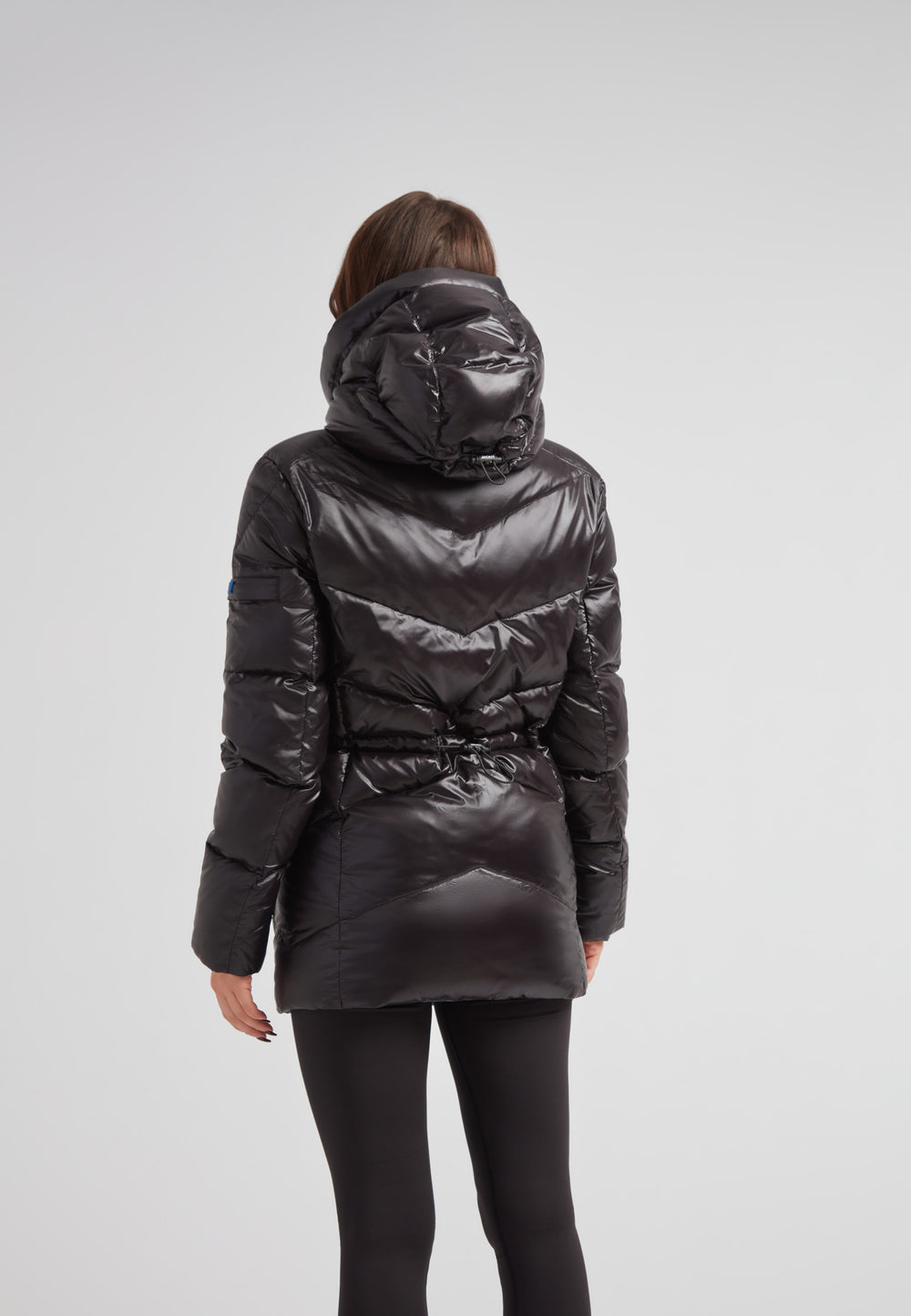 Back view of a woman wearing the black thigh-length womens slick coat with a hood and cinched waist.