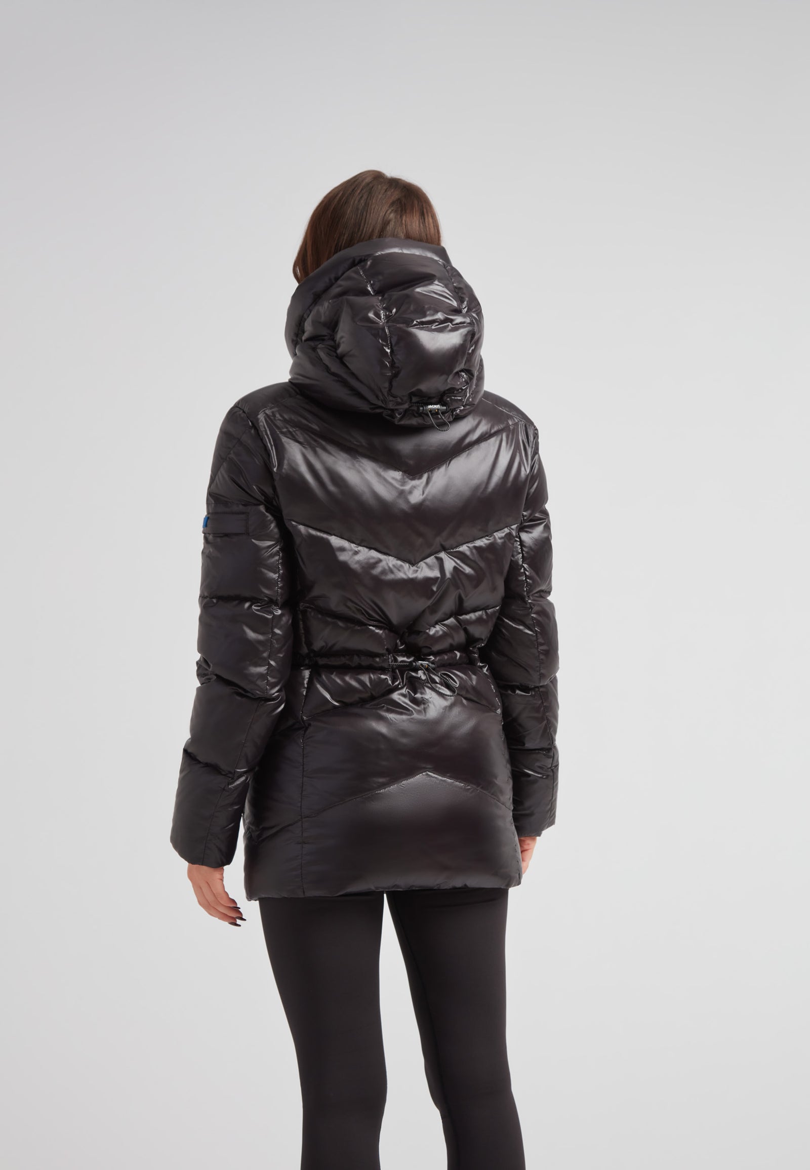 Back view of a woman wearing the black thigh-length womens slick coat with a hood and cinched waist.
