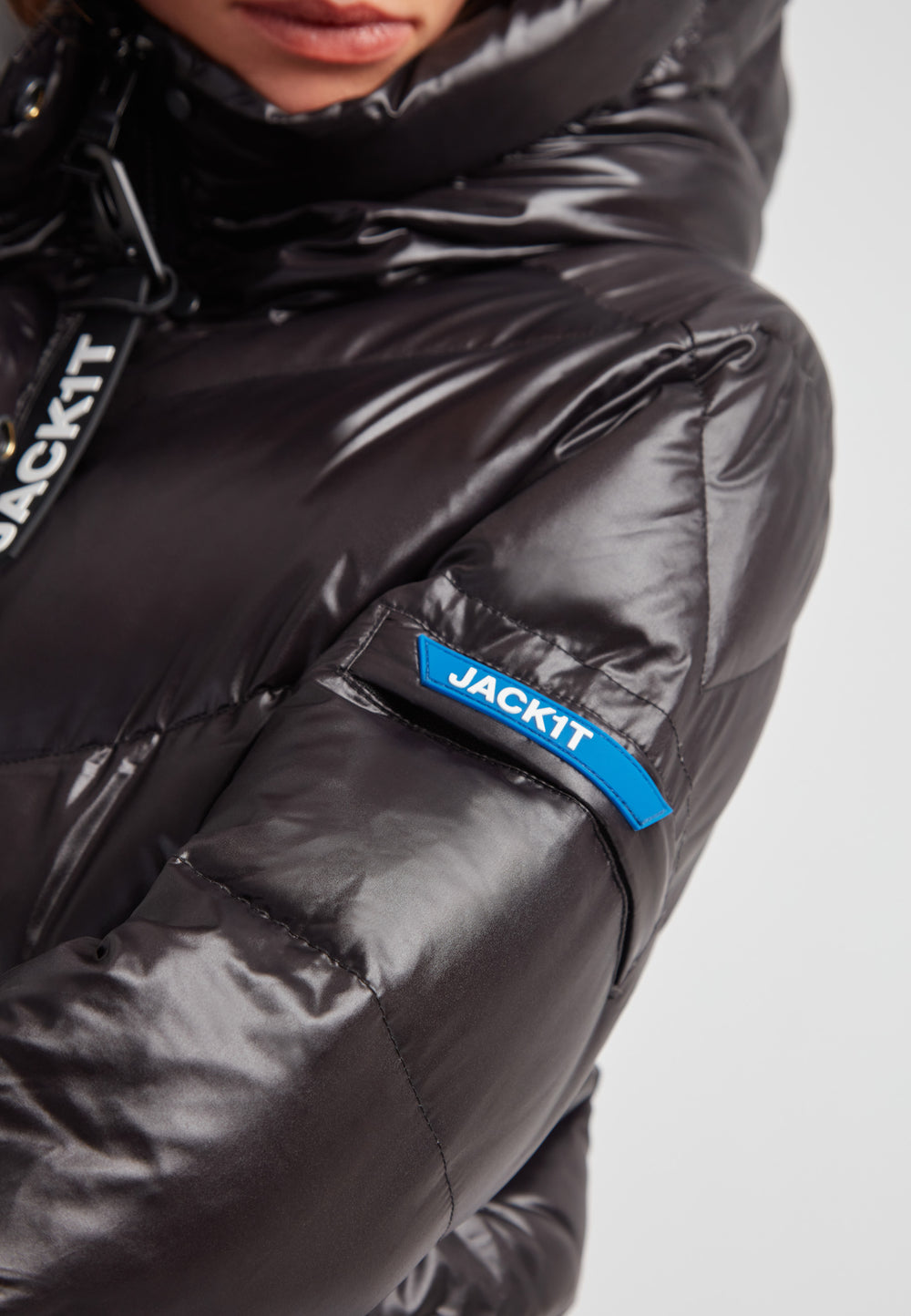 Close-up of the EZ Frontier Prime Down Puffer Coat showcasing the shiny black material and brand logo. Black thigh-length womens slick coat.