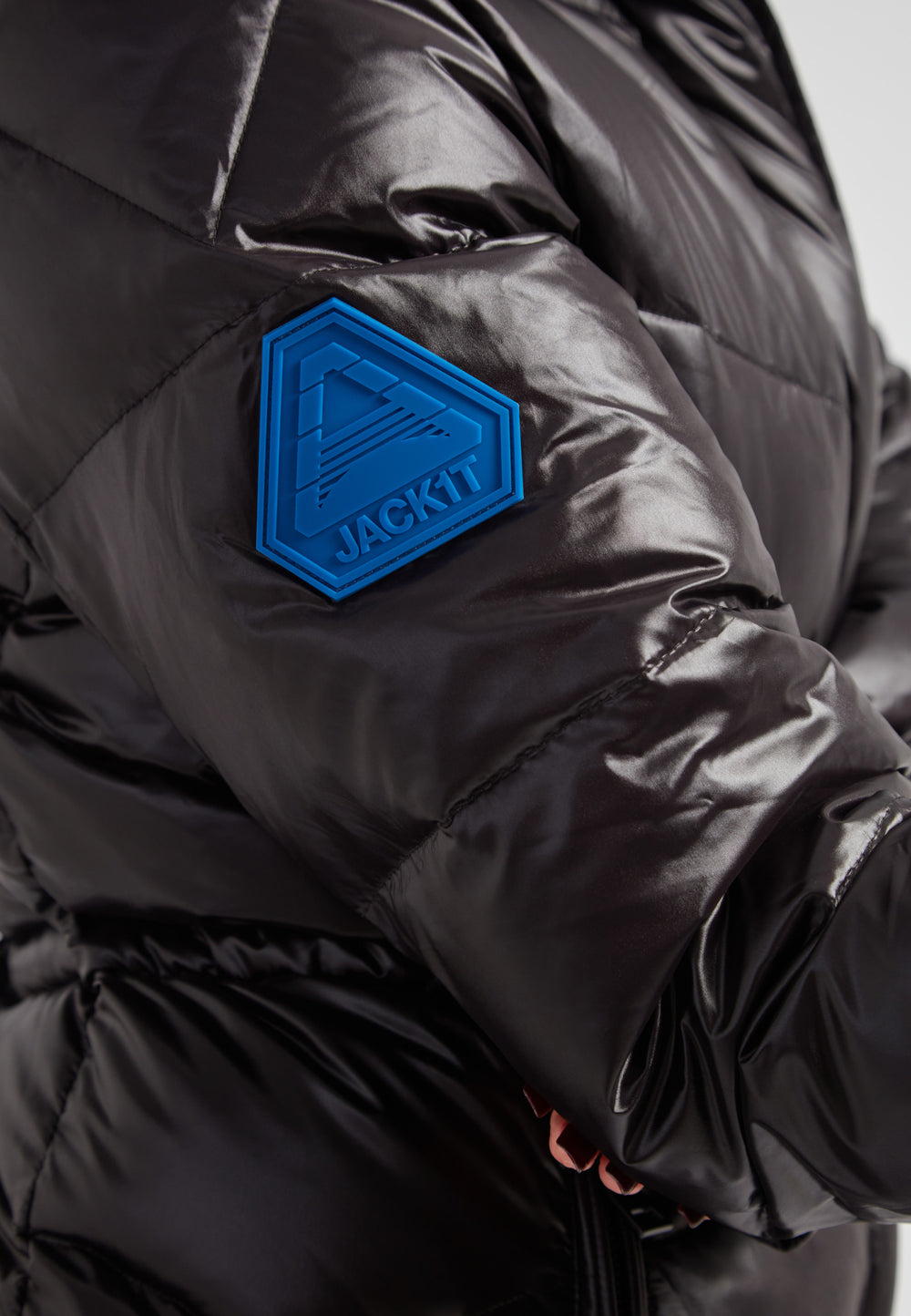 Close-up of the arm of the EZ Frontier Prime Down Puffer Coat featuring the JACKIT logo on a black thigh-length womens slick coat.