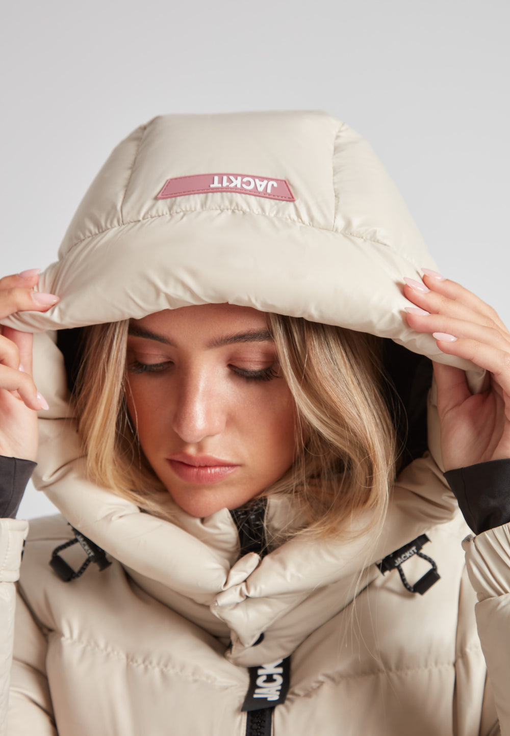 Close-up of a woman wearing the EZ Belted Down Puffer Coat Lux Stone with hood, showcasing its stylish design and comfort.