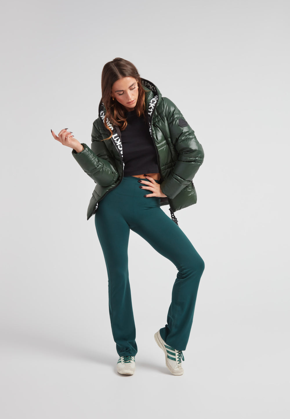 Woman wearing R4D Tramline Puffer Racer Jacket Lux Emerald with sporty pants, posing confidently against a neutral backdrop.