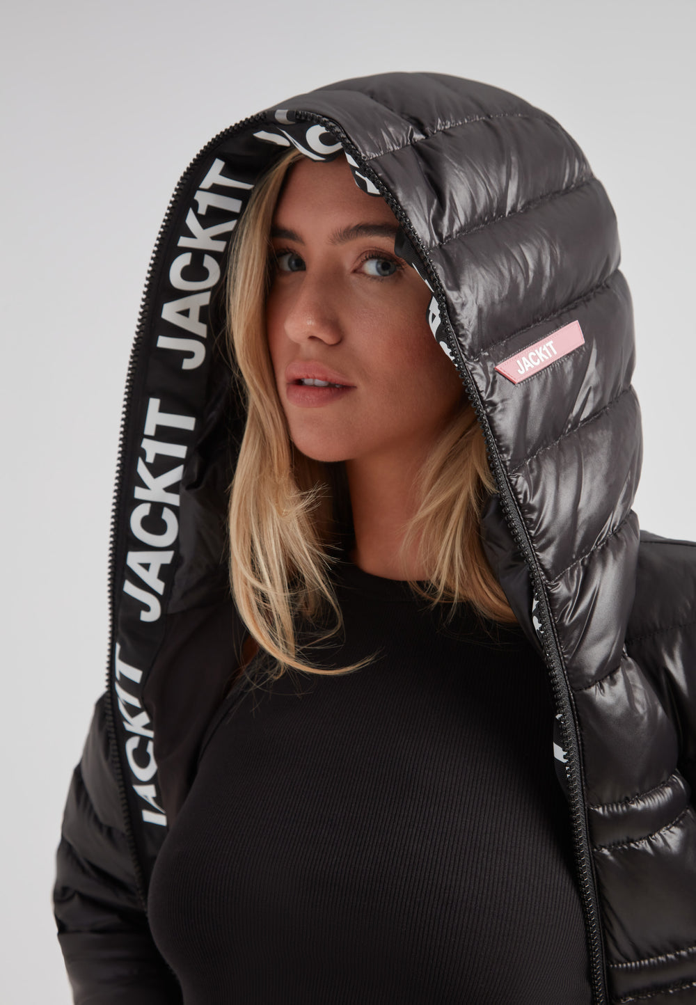 Woman wearing the R4D Tramline Down Coat Lux Black with hood up, showcasing elegant design and JACK1T branding.