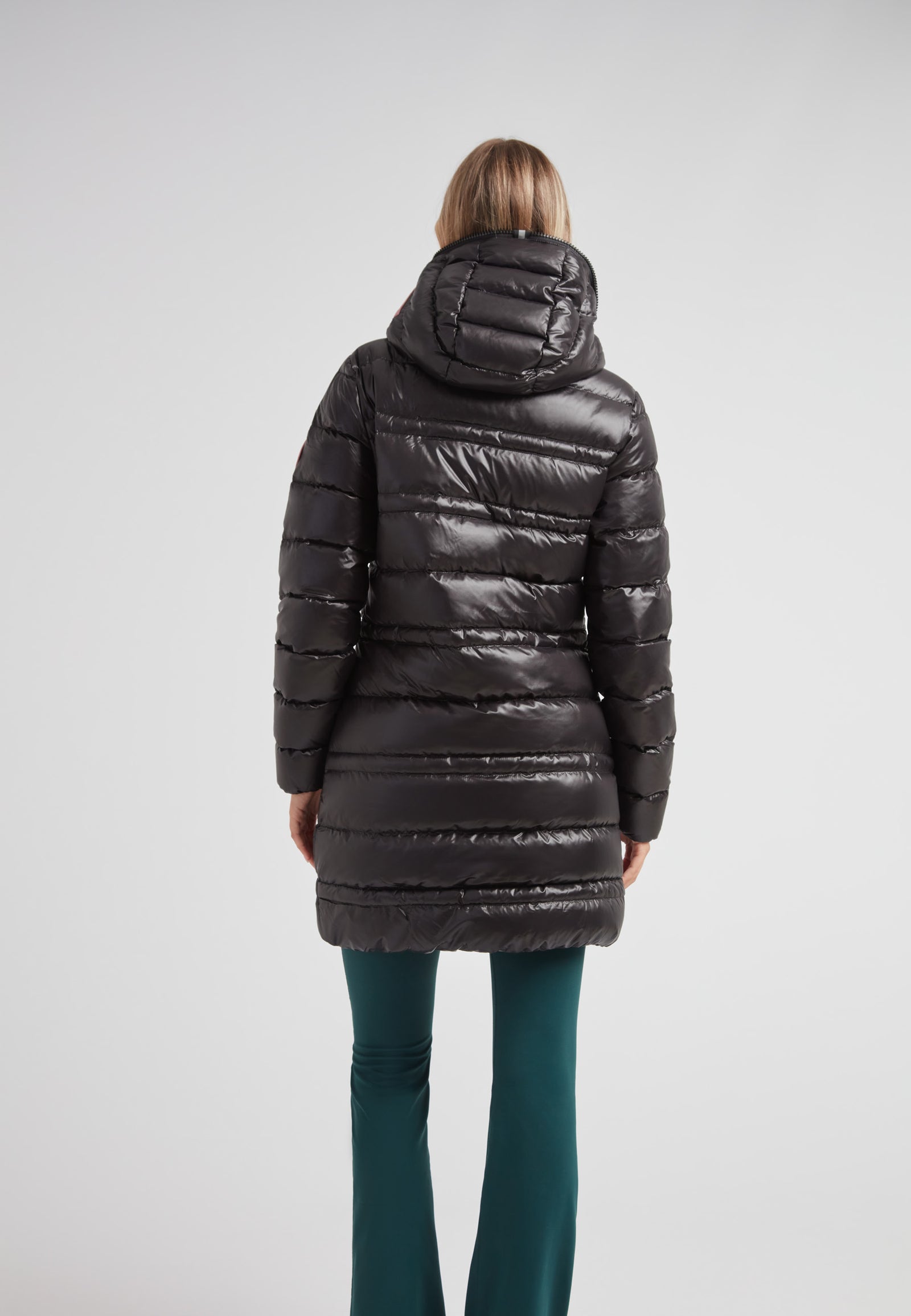 R4D Tramline Down Coat Lux Black worn by a woman, showcasing the back view with a sleek design and hood.