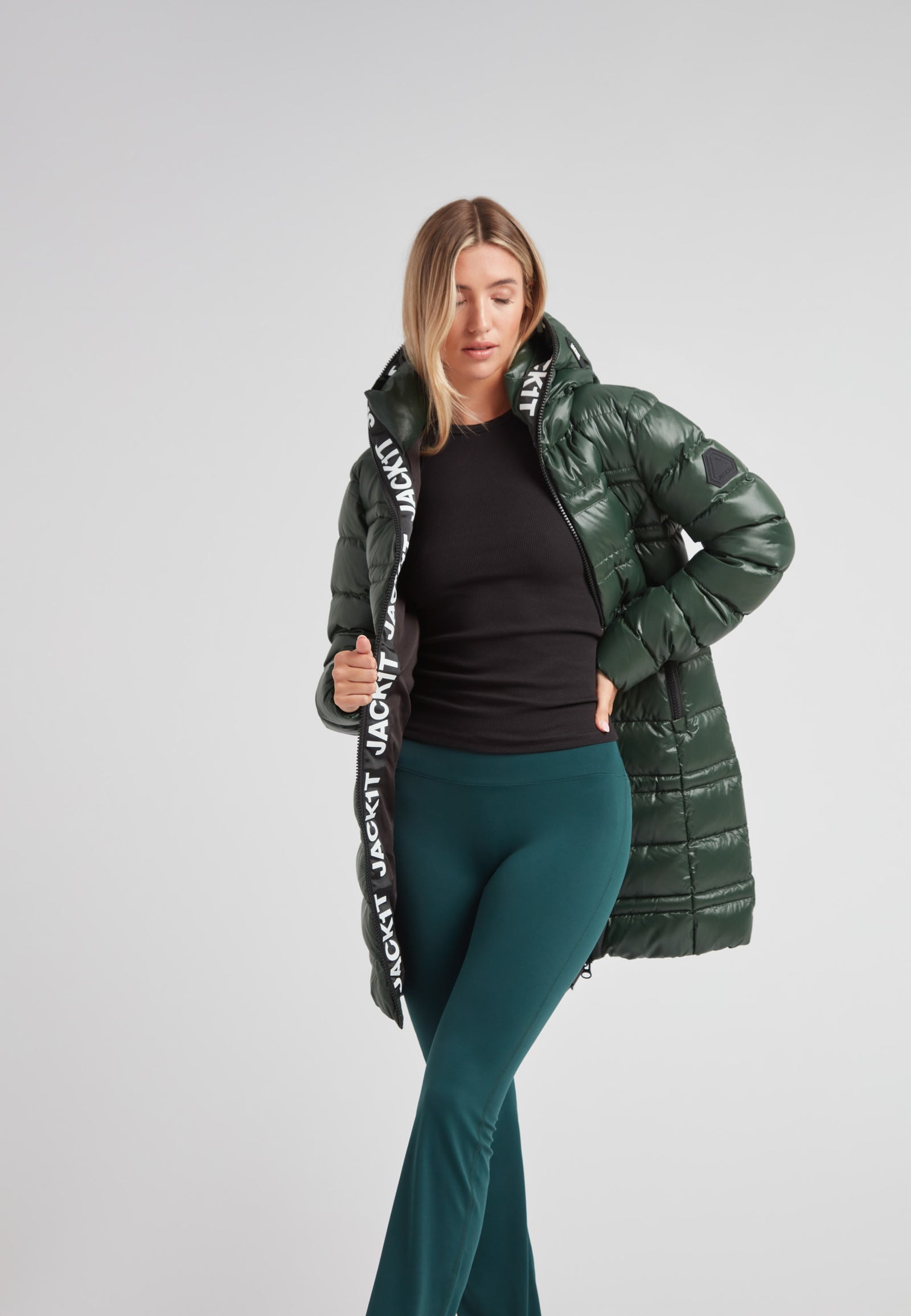 Woman wearing R4D Tramline Down Coat Lux Emerald in green with black pants, showcasing stylish winter outerwear.