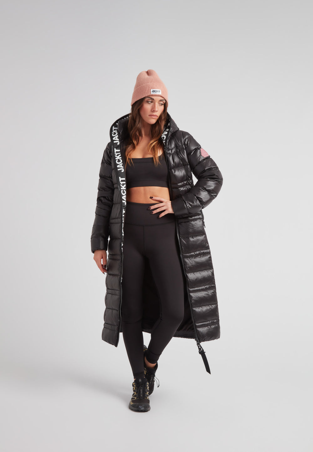 R4D Tramline Extra Long Down Coat Lux Black with hood and side zip, worn by model in black leggings and pink beanie.
