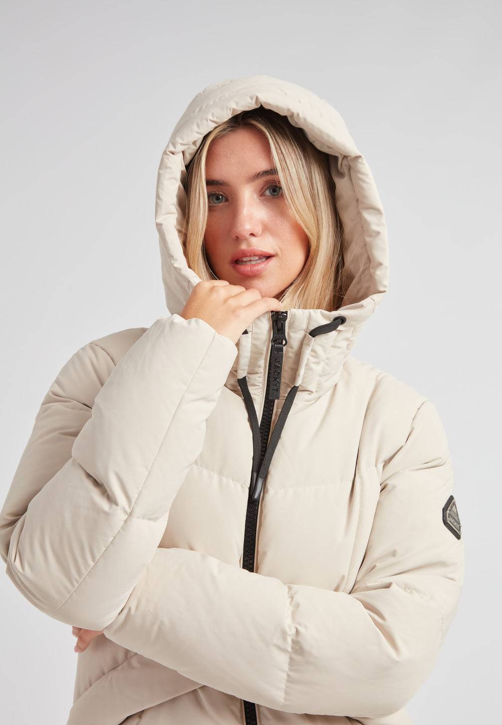 Black Star Puffer Down Coat Stone model wearing a beige hooded winter coat indoors.