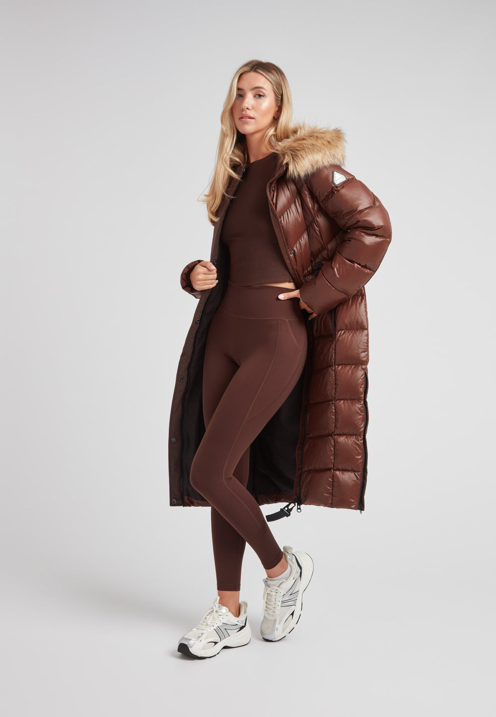 Women's puffer coat with fur hood in brown, styled in a full-length look with a matching outfit.