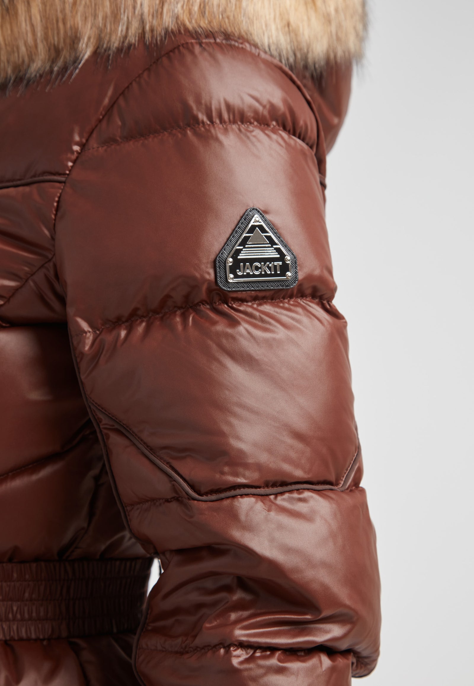 Women's puffer coat with fur hood in brown showcasing quilted sleeve detail and branded patch.