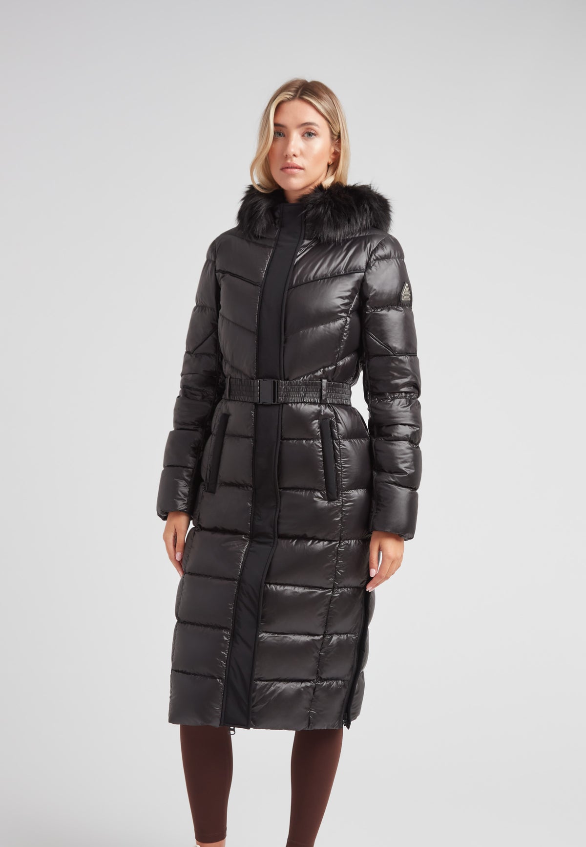 Women's puffer coat with fur hood in black, featuring a belted waist and full-length silhouette.