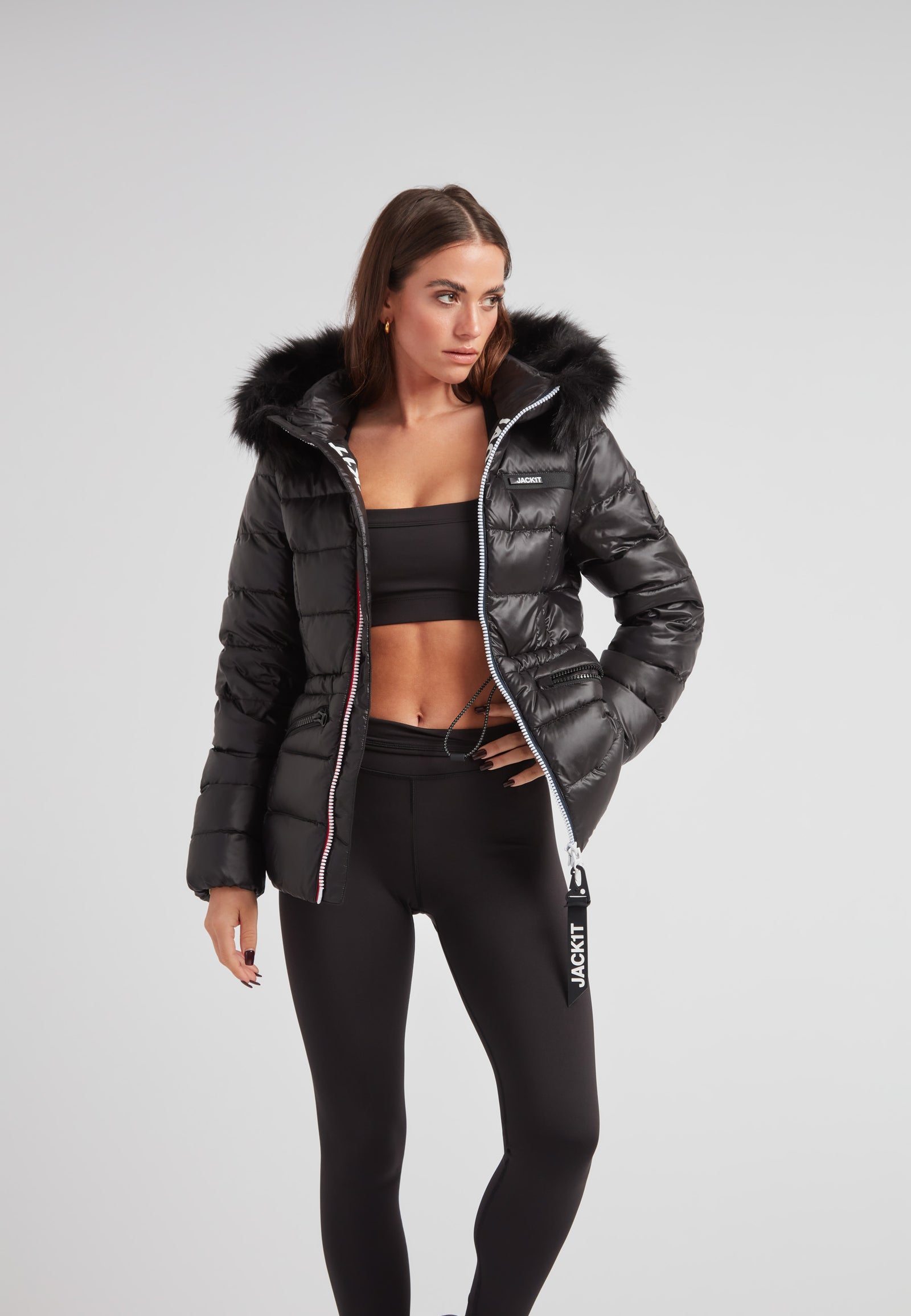Black racer puffer jacket with fur hood worn by a woman, featuring precision tailoring and modern ski styling.