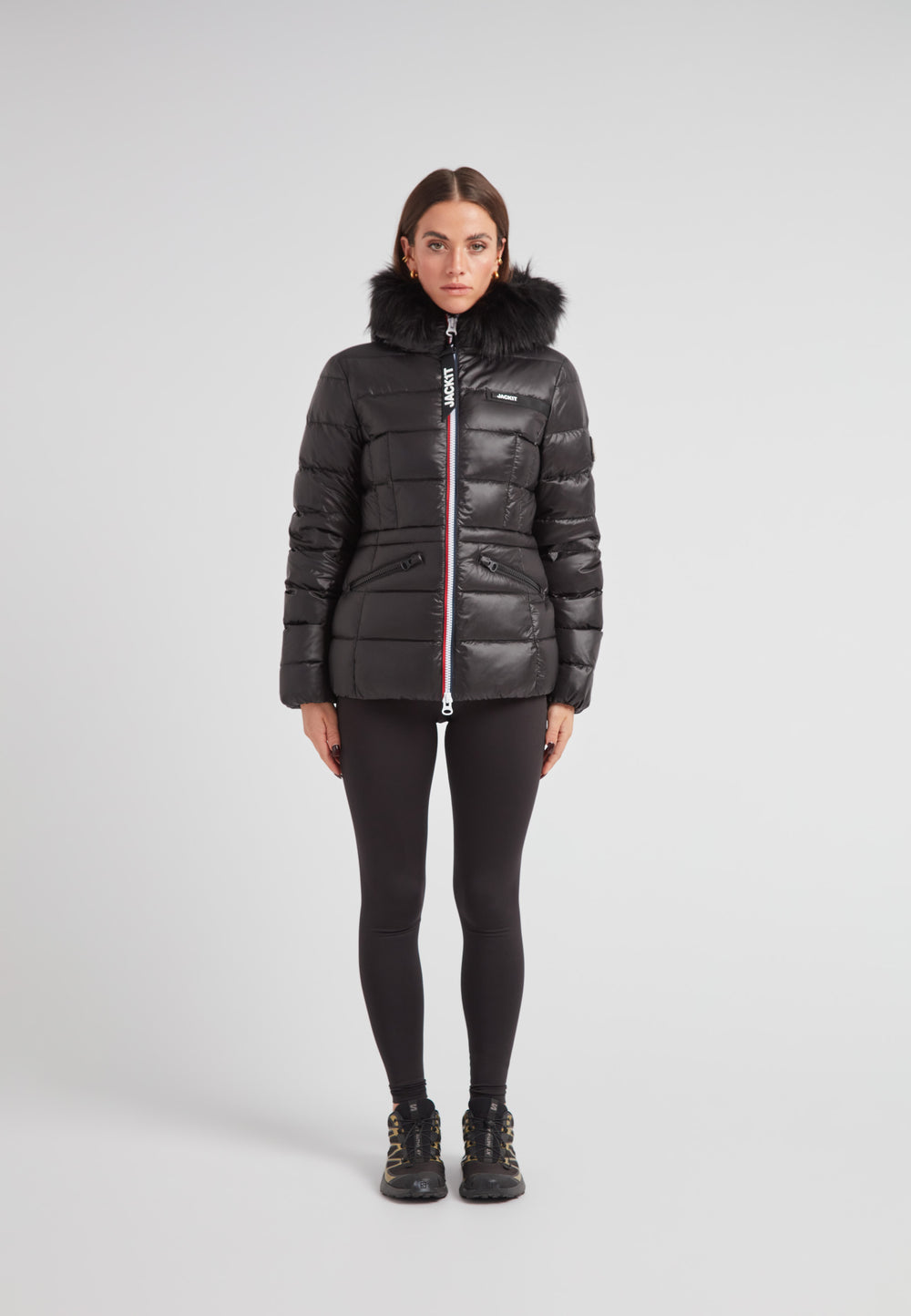 Black racer puffer jacket with fur hood worn by a model standing against a neutral background.