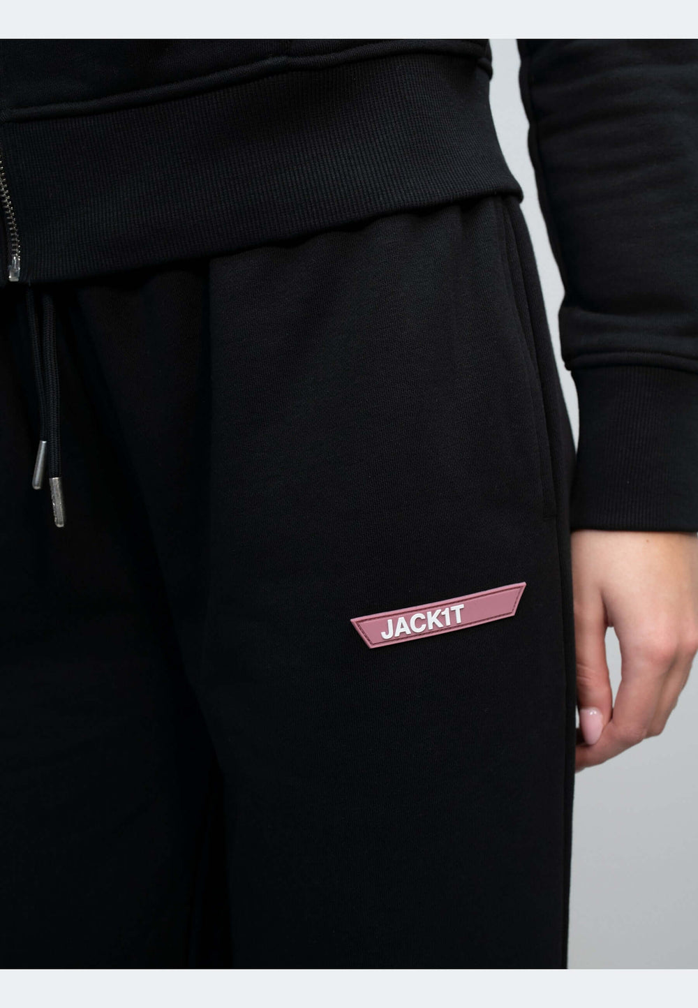 Close-up of a person wearing black joggers with a pink JACKIT logo on the side.