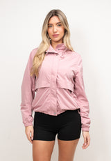Model wearing a women's pink windbreaker in dusty pink, showcasing lightweight design and stow-away hood.