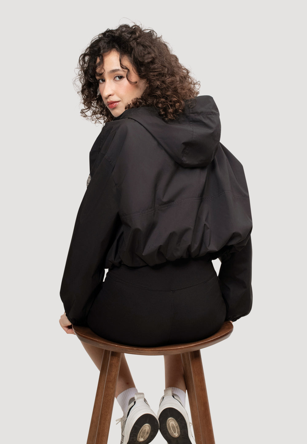 Back view of a model wearing a women's black cropped jacket, showcasing its relaxed fit and hood.