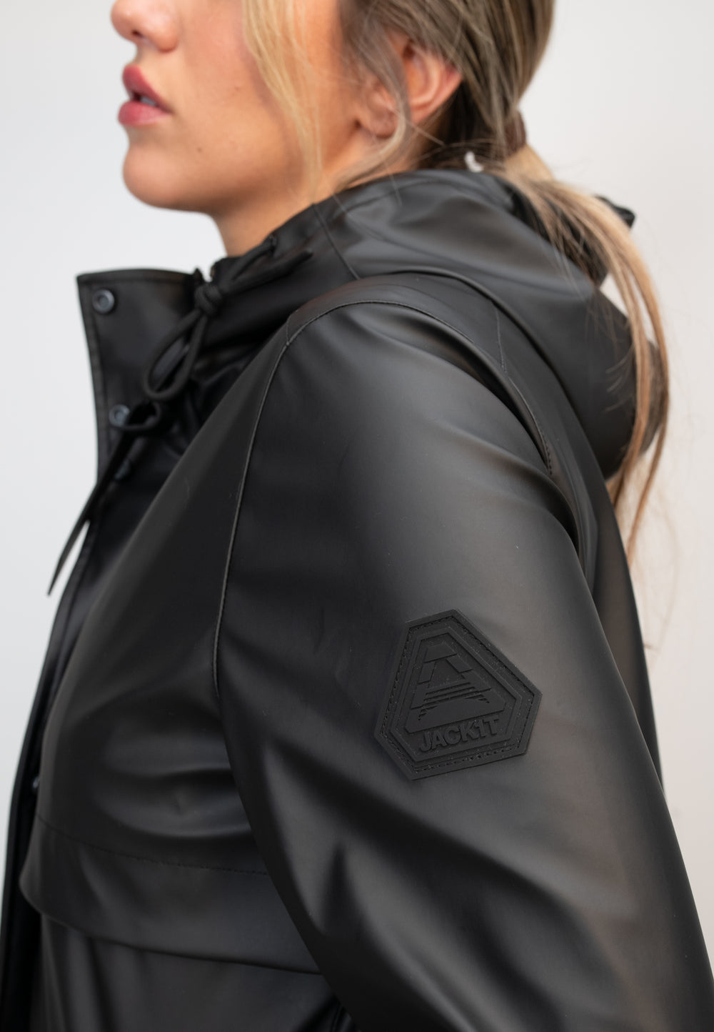 Close-up of a woman wearing a lightweight women's black raincoat with a hood and logo detail.
