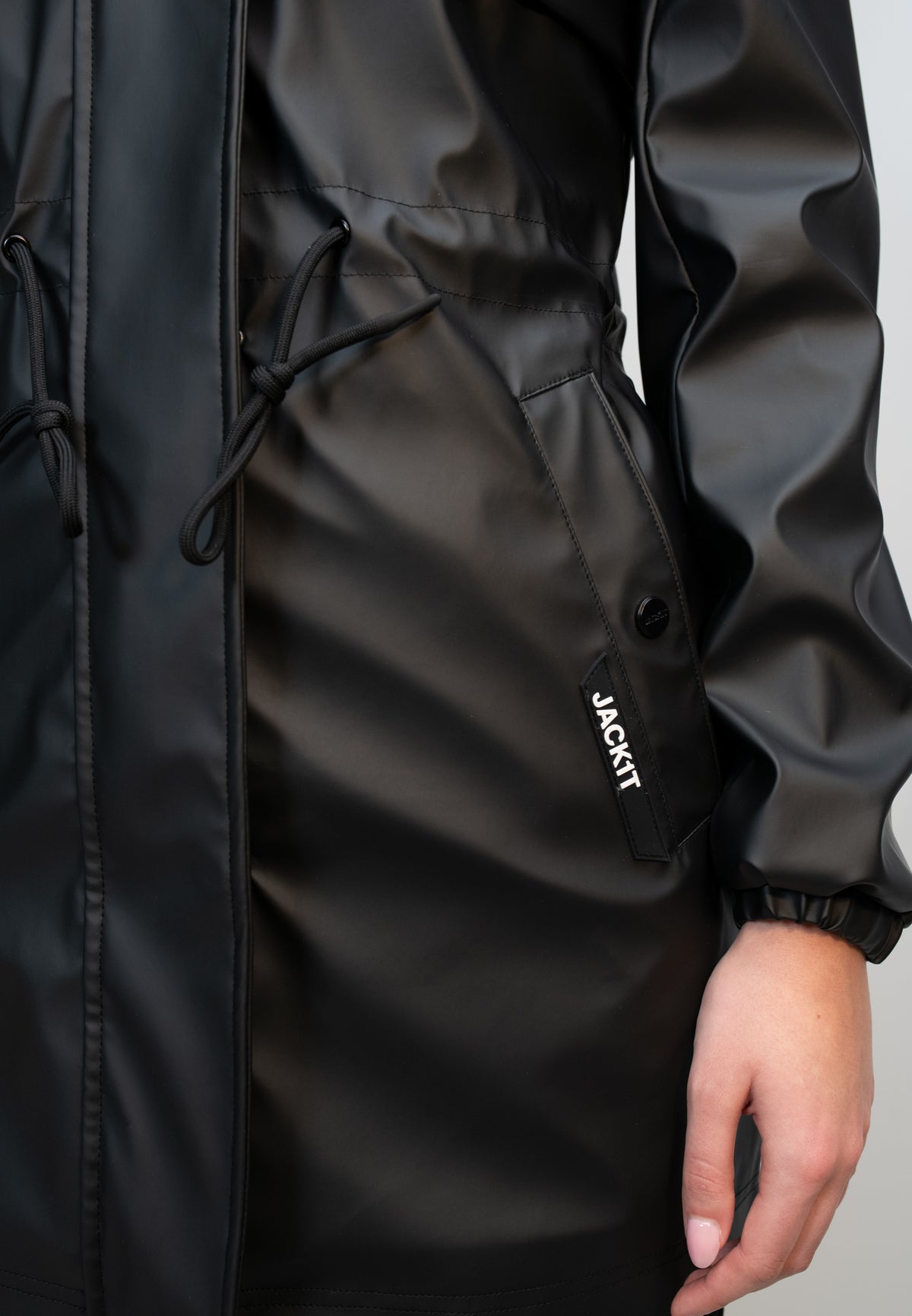 Close-up of women's black raincoat with cape and pockets, showcasing the lightweight, water-resistant material and details.