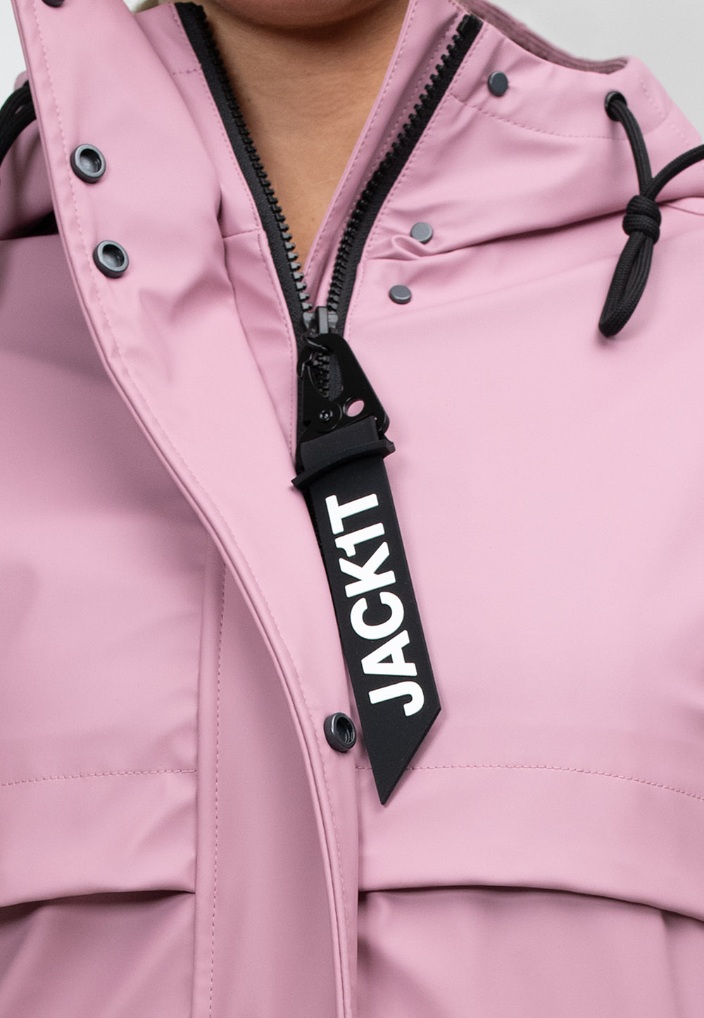 Close-up of a women's pink raincoat with a hood and zipper detailing, showcasing the JACKIT brand label.