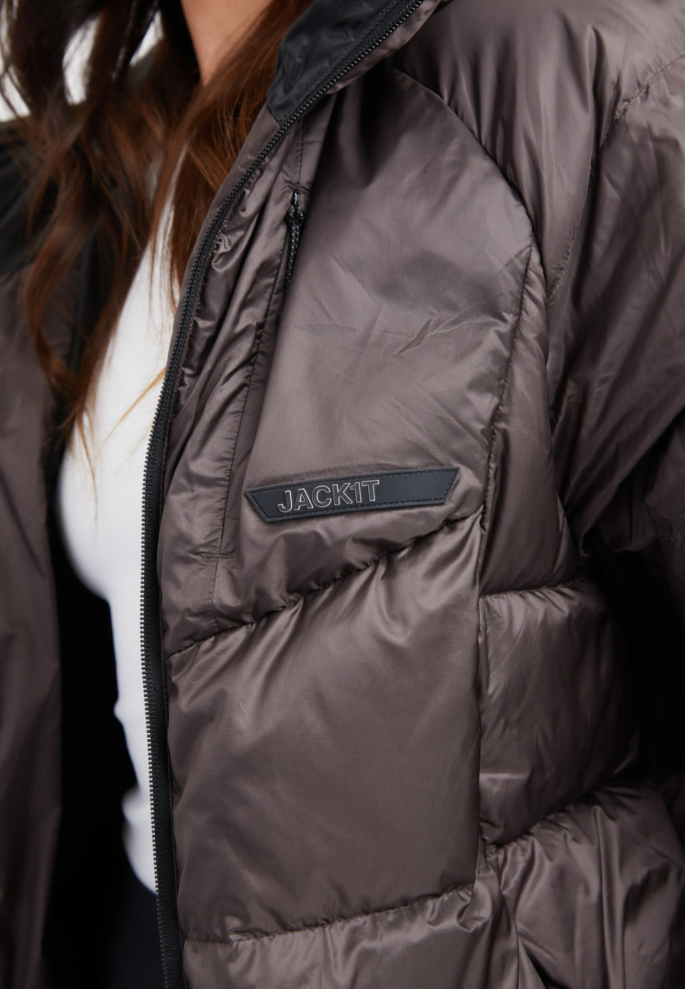Close-up of an oversized puffer brown jacket featuring a black patch logo on the chest.