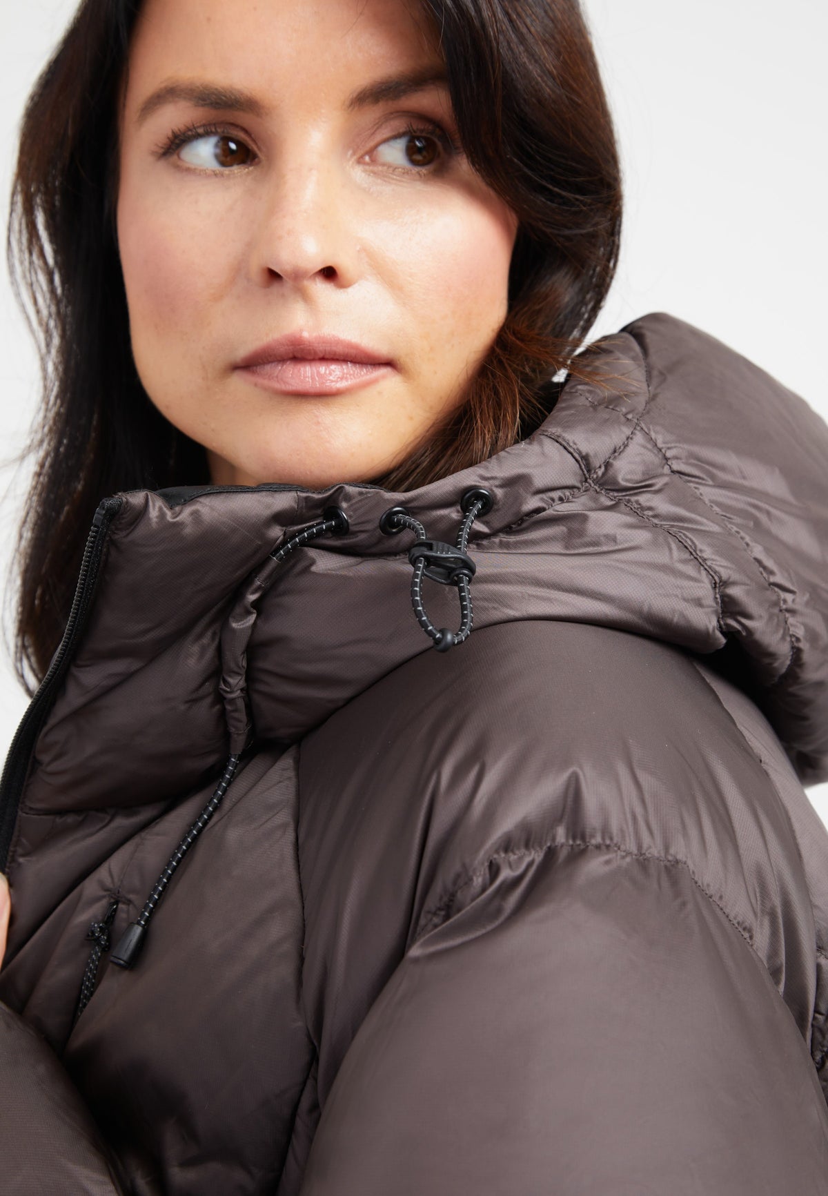 Close-up of a woman wearing an oversized puffer brown jacket with an adjustable hood.