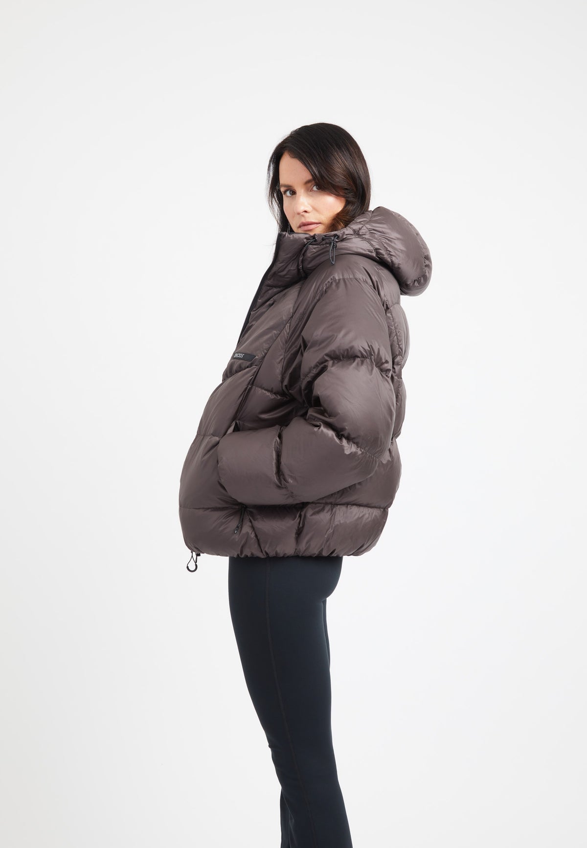 Woman wearing an oversized puffer brown bubble jacket in mid brown color, showcasing modern design and adjustable hood.