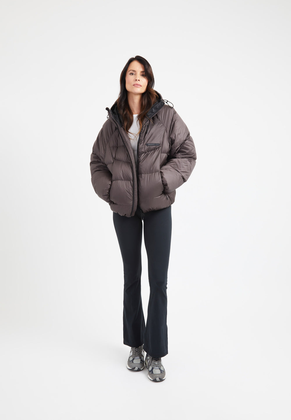 Model wearing oversized puffer brown jacket with adjustable hood and fleece lined pockets.
