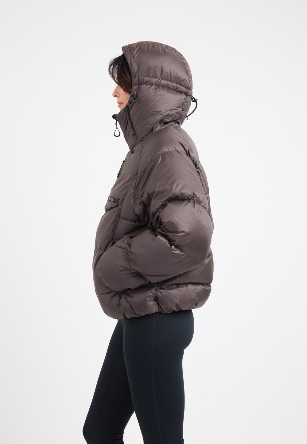 Side view of an oversized puffer brown jacket with an adjustable hood and dark fabric, ideal for winter wear.