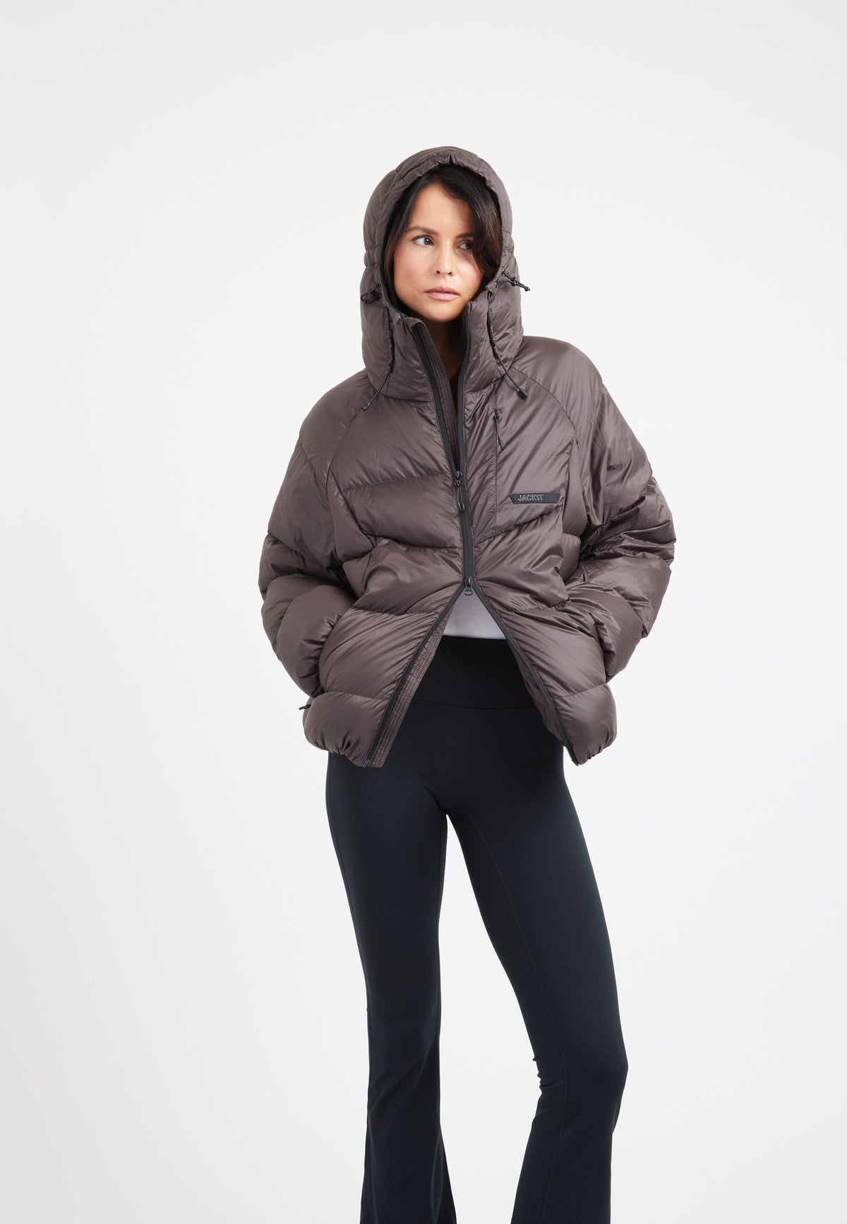 Woman wearing an oversized puffer brown jacket with an adjustable hood and black leggings.