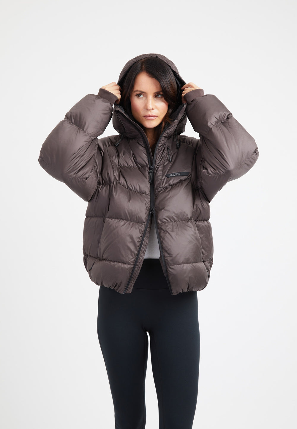 Model wearing an oversized puffer brown bubble jacket with a hood and fleece lined pockets.