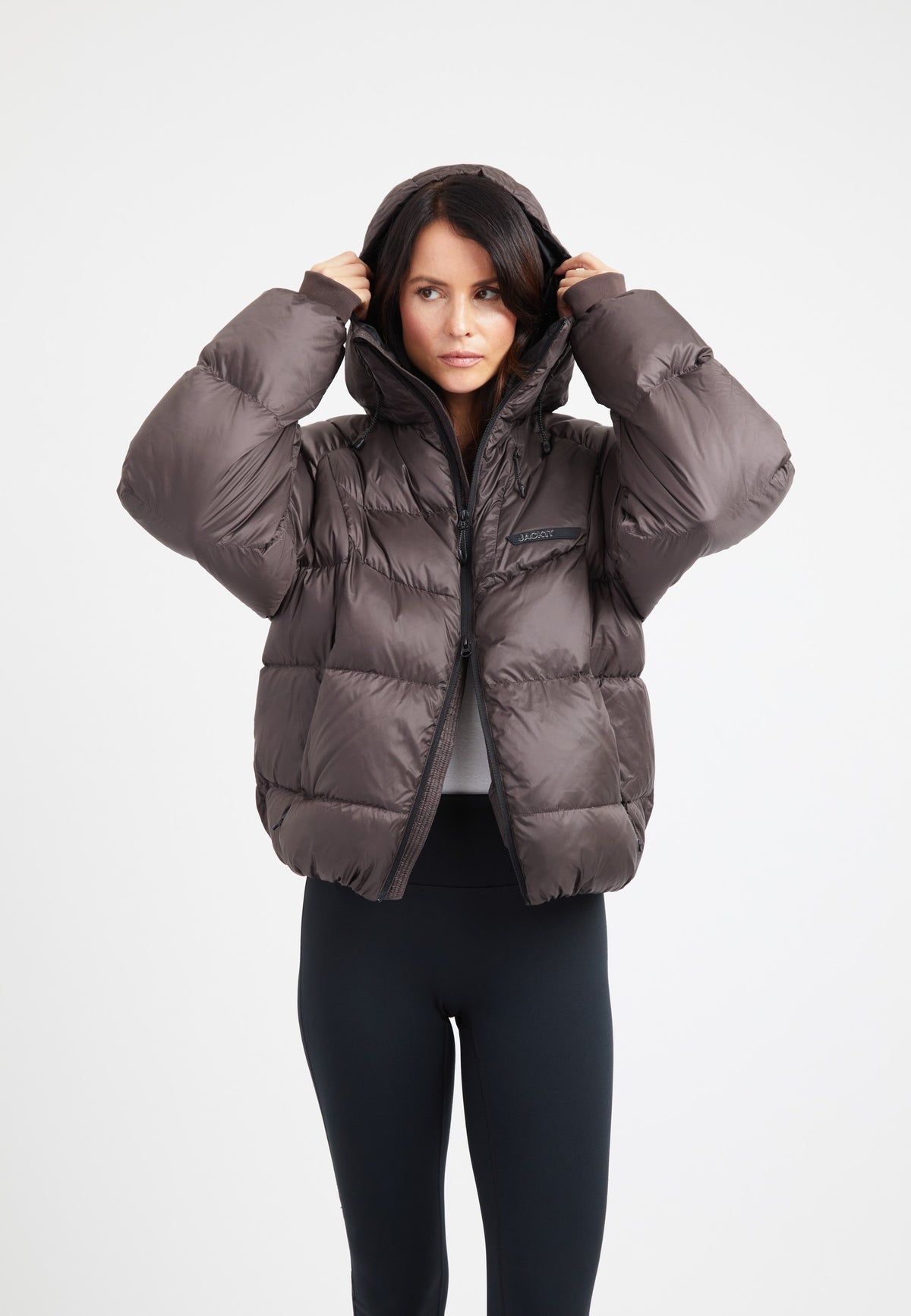 Model wearing an oversized puffer brown bubble jacket with a hood and fleece lined pockets.