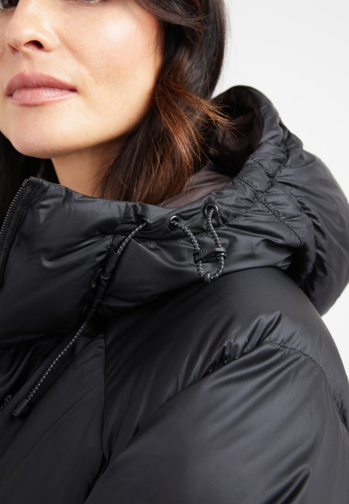 Close-up of a woman wearing an oversized puffer black jacket with an adjustable hood.