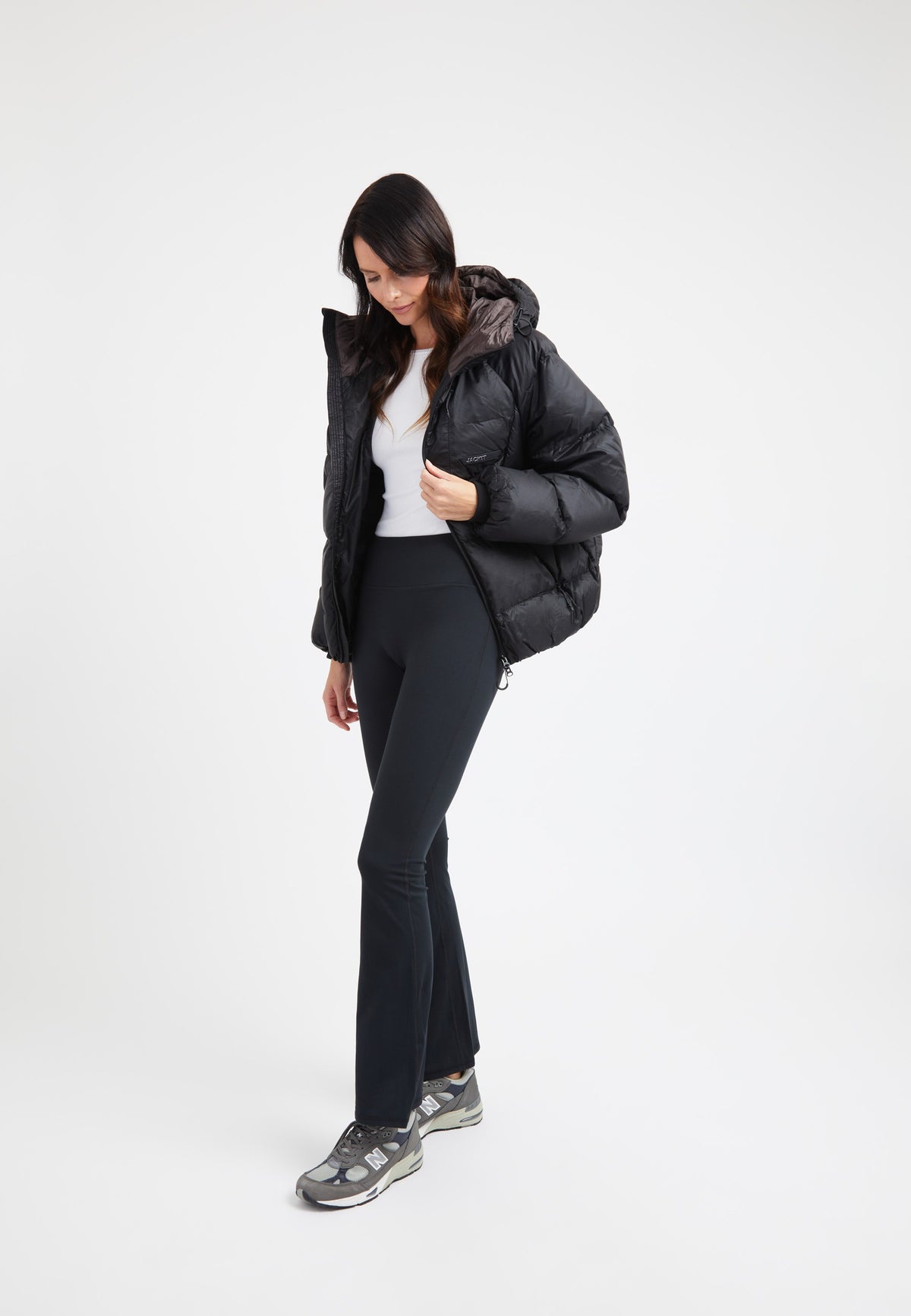 Model wearing an oversized puffer black jacket with a hood, styled with black pants and sporty shoes.
