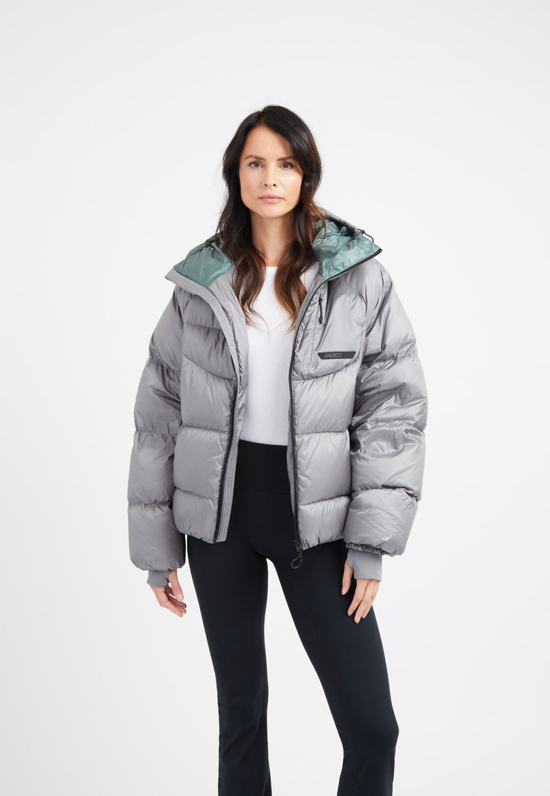 Model wearing an oversized puffer grey jacket with adjustable hood and fleece lined pockets.