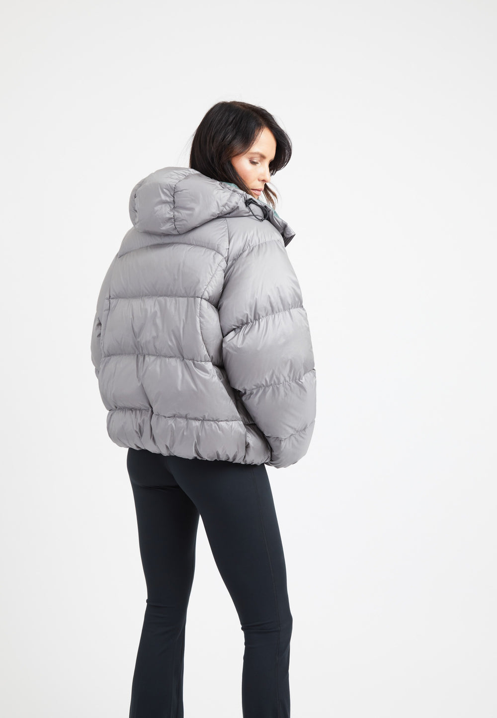 Woman showcasing oversized puffer grey jacket with hood, back view against a plain background.