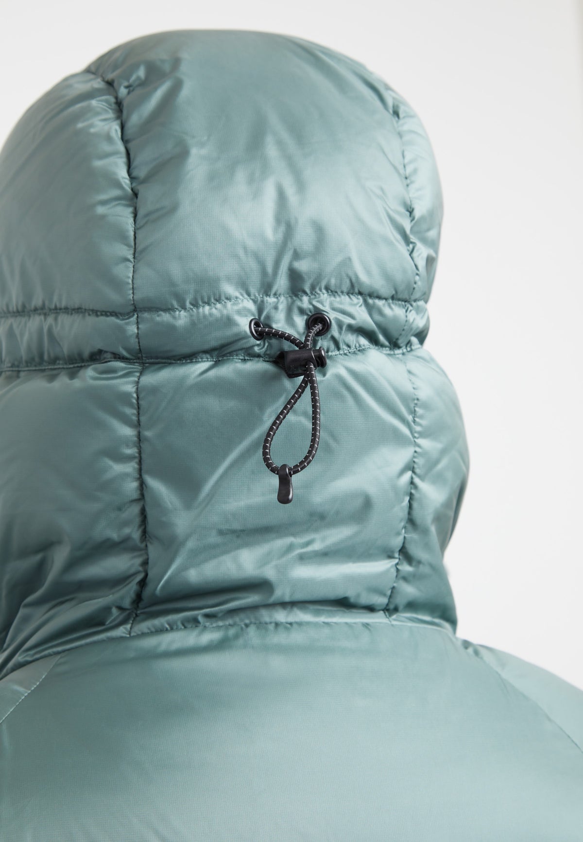 Detail of the adjustable hood on an oversized puffer green jacket, showcasing the fabric and drawstring.
