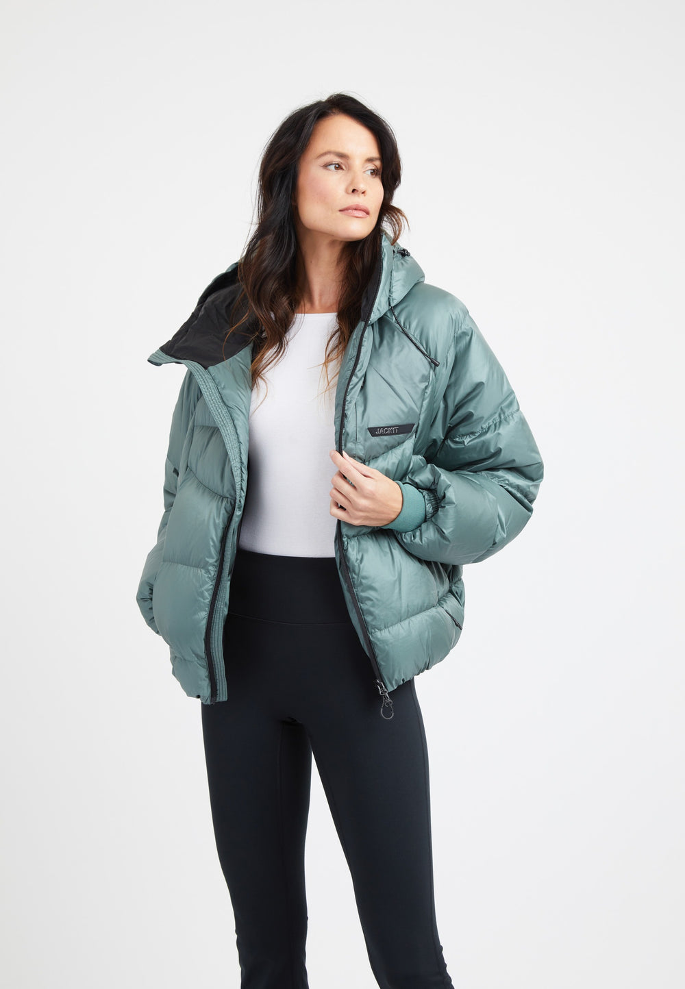 Model wearing an oversized puffer green jacket styled with black leggings and a white top against a plain background.