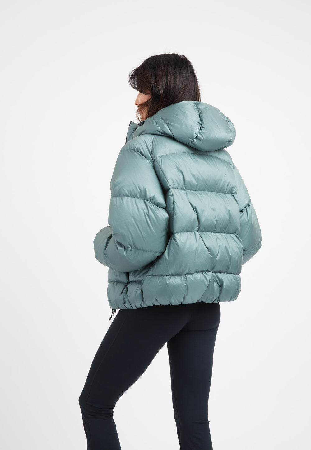 Woman wearing an oversized puffer green jacket, featuring an adjustable hood and modern silhouette.