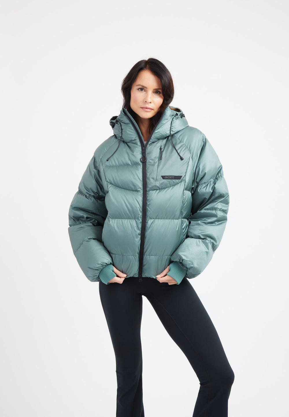 Woman wearing an oversized puffer green jacket with adjustable hood and fleece-lined hand pockets.
