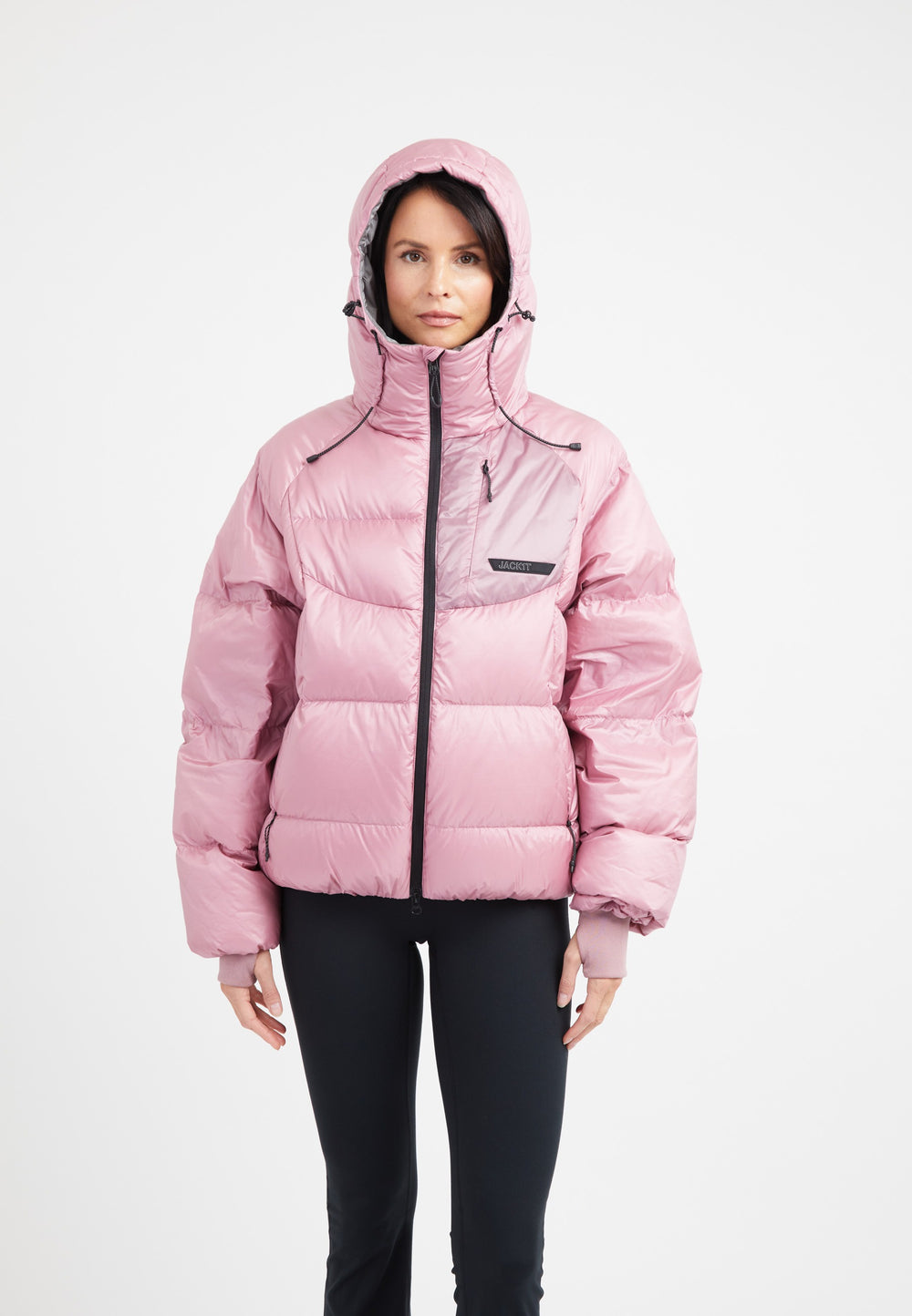 Woman wearing an oversized puffer in pink, featuring adjustable hood and fleece lined pockets.