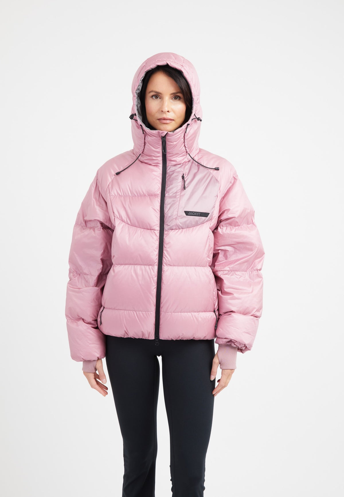 Woman wearing an oversized puffer in pink, featuring adjustable hood and fleece lined pockets.