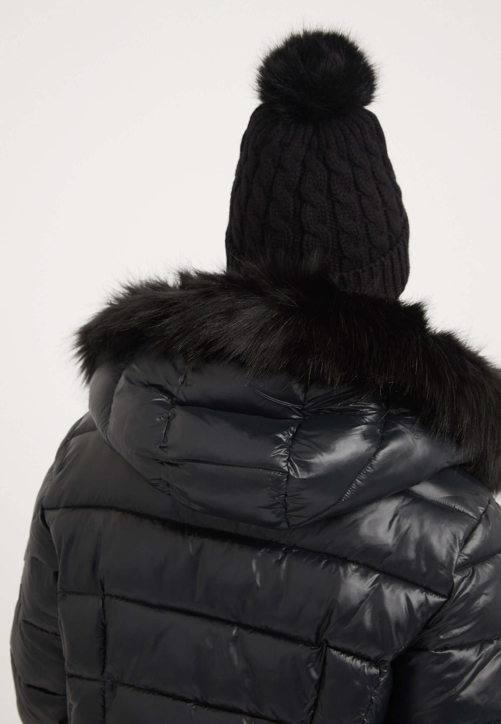 Back view of a black womens puffer jacket with faux-fur trim and knitted beanie hat.