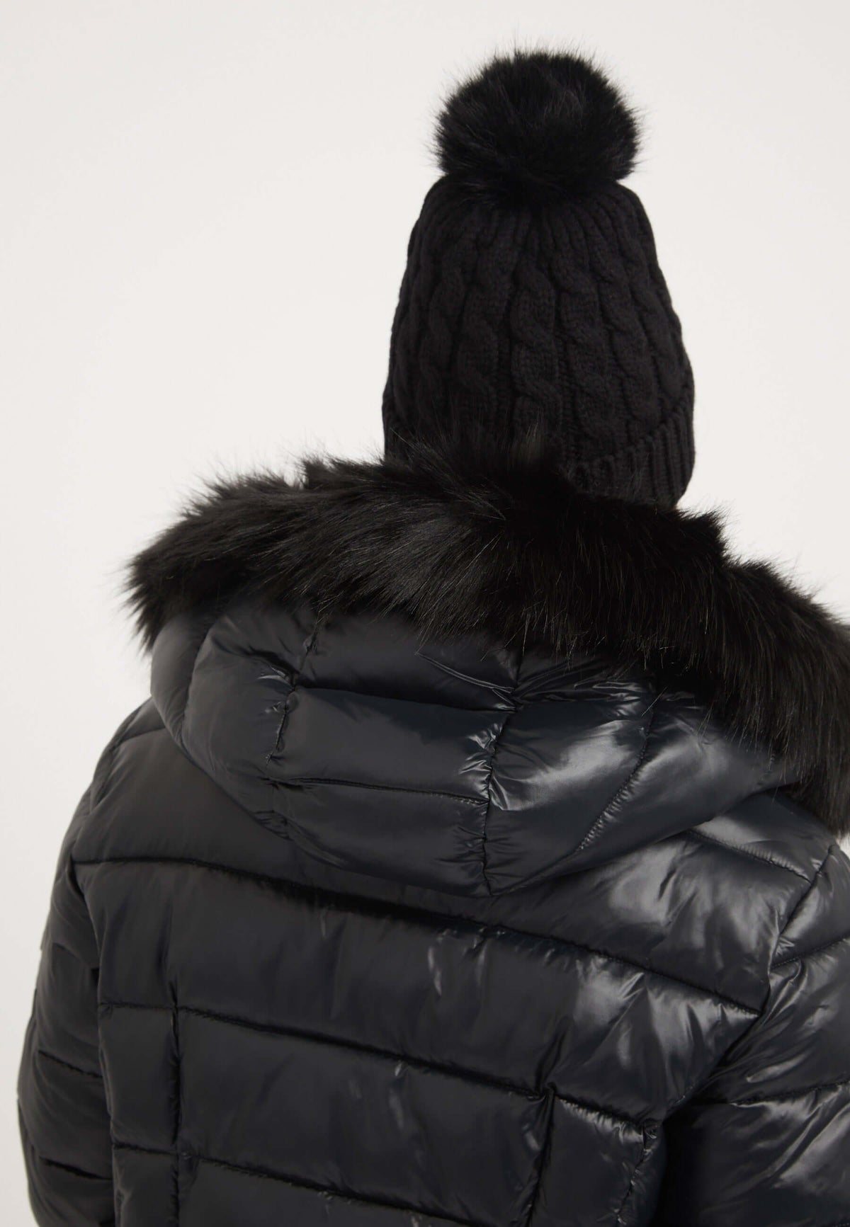 Back view of a black womens puffer jacket with faux-fur trim and knitted beanie hat.